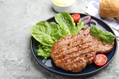 Lezzetli hamburger köfteleri, domates, marul, çörekler ve baharatlar gri masada, yakın plan. Metin için boşluk