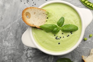 Lezzetli bezelye kremalı çorba fesleğen ve kızarmış ekmek gri masada servis edilir.