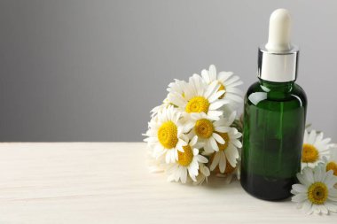 Bir şişe gerekli yağ ve papatya çiçekleri açık ahşap masada gri arka planda, yakın plan. Metin için boşluk