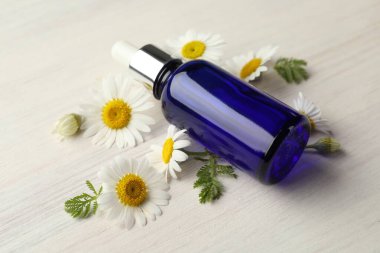 Bir şişe gerekli yağ ve papatya çiçekleri açık ahşap masada, yakın plan.