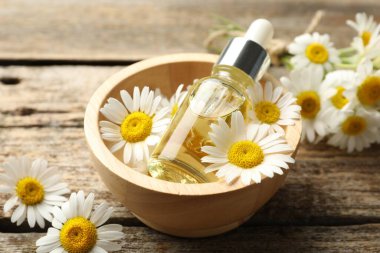 Ahşap masada bir şişe yağ ve papatya çiçeği, yakın plan.