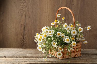 Hasır sepetin içinde güzel papatya çiçekleri ahşap masanın üzerinde, metin için yer var.