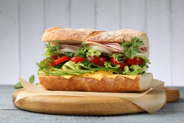 Gri ahşap masada jambonlu, peynirli ve sebzeli lezzetli baget sandviç.