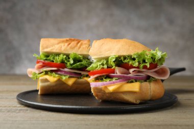 Jambonlu, peynirli ve sebzeli lezzetli baget sandviçler ahşap masada, yakın plan, gri arka plan...