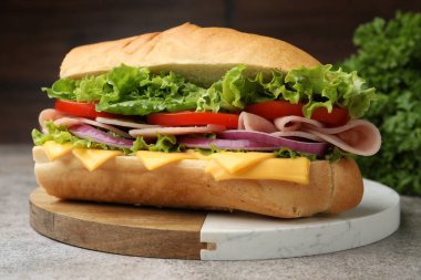 Gri desenli masada jambonlu, peynirli ve sebzeli baget sandviç, bulanık kahverengi arka plan, yakın plan.