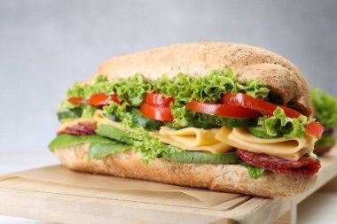 Lezzetli baget sandviç, füme sosis, peynir ve sebzeler beyaz masada, yakın plan.