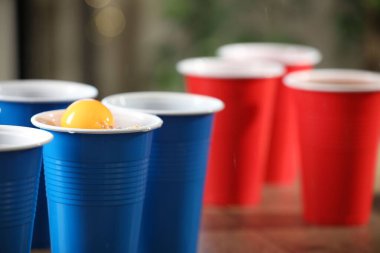 Bira pong oyunu. İçkili plastik bardaklar ve tahta masanın üzerinde top, yakın plan. Metin için boşluk