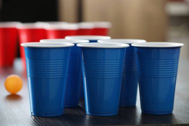 Bira pong oyunu. İçkili plastik bardaklar ve tahta masada top, yakın plan.