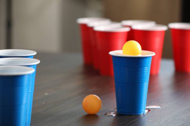 Bira pong oyunu. İçkili plastik bardaklar ve toplar ahşap masada, yakın plan.