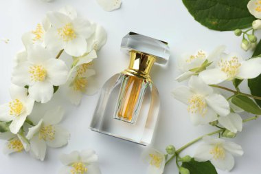 Bir şişe parfüm, yasemin çiçekleri ve beyaz arka planda yeşil yapraklar.