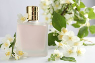 Beyaz masada bir şişe parfüm ve yasemin çiçeği, yakın plan.
