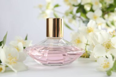 Beyaz masada bir şişe parfüm ve yasemin çiçeği, yakın plan.