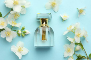 Bir şişe parfüm ve açık mavi arka planda güzel yasemin çiçekleri.