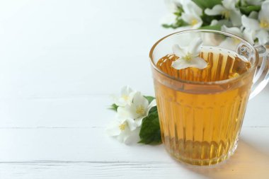 Cam bardakta Aromatik yasemin çayı, beyaz tahta masada çiçekler ve yeşil yapraklar, yakın plan. Metin için boşluk