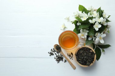 Cam bardakta Aromatik yasemin çayı, beyaz ahşap masada çiçekler ve yapraklar, düz yatış. Metin için boşluk