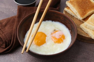 Kavanozda yarı haşlanmış yumurta, yemek çubuğu, soya sosu ve kahverengi masada kızarmış ekmek, yakın plan.