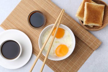 Yarısı kaynamış yumurta, soya sosu, yemek çubukları, kahve ve kızarmış ekmek açık gri masada, düz yatıyordu.