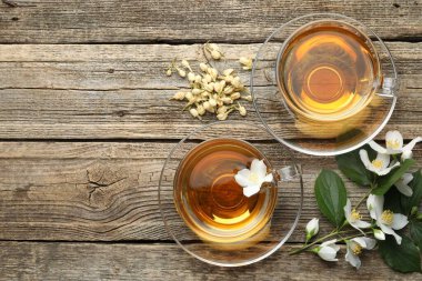 Cam bardaklarda yasemin çayı, tahta masada çiçekler ve yeşil yapraklar, düz yatak. Metin için boşluk