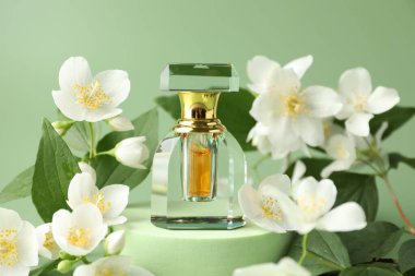 Yeşil arka planda bir şişe parfüm ve yasemin çiçeği, yakın plan.