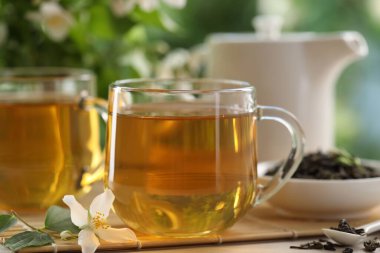 Lezzetli yasemin çayı fincanlar, çaydanlık, kuru yapraklar ve çiçekler beyaz ahşap masada, yakın plan.