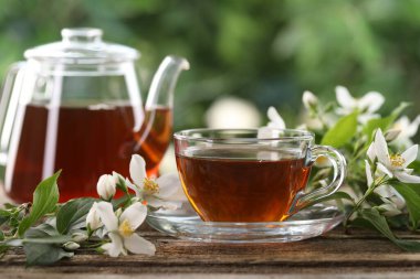 Lezzetli yasemin çayı fincanda, çaydanlık ve çiçekler ahşap masada, yakın plan