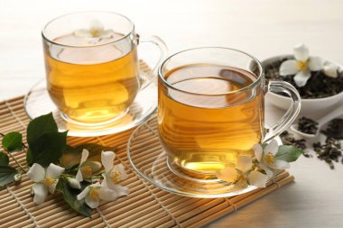 Lezzetli yasemin çayı, kuru yapraklar ve beyaz ahşap masa üzerinde çiçekler, yakın plan.