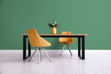 Yemek masası ve turuncu sandalyeler yeşil duvarın yanında. İç tasarım