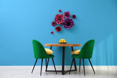 Yemek masası ve açık mavi duvarın yanında yeşil sandalyeler. Odada çiçek dekoru var. İç tasarım