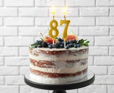 Meyveli lezzetli pasta ve beyaz tuğla duvarın yanında yanan mumlar. 87. yaş günü veya diğer özel günler