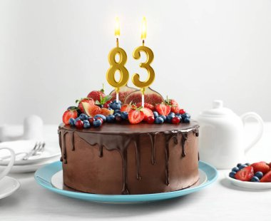 Meyveli çikolatalı kek ve beyaz masada yanan mumlar. 83. Doğum günü veya diğer özel günler