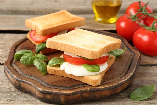 Mozarella peynirli, domatesli ve ahşap masadaki fesleğenli lezzetli sandviçler.