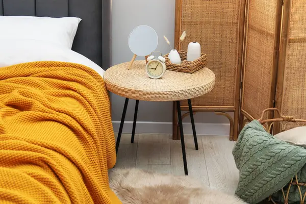 Yan masada ayna, çalar saat ve yatağın yanında dekor var.