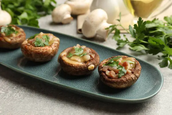Eritilmiş peynirli ve maydanozlu lezzetli mantarlar. Gri desenli masa, yakın plan.