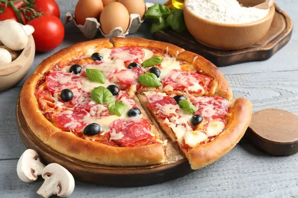 Lezzetli pizza ve malzemeler gri ahşap masada, yakın plan.