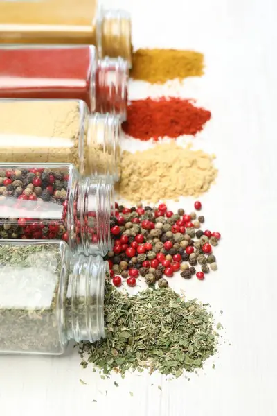 Beyaz masadaki kavanozlarda farklı aromatik baharatlar, yakın plan.