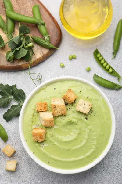 Gri masada servis edilen kıtır ekmekli bezelye kremalı çorba.