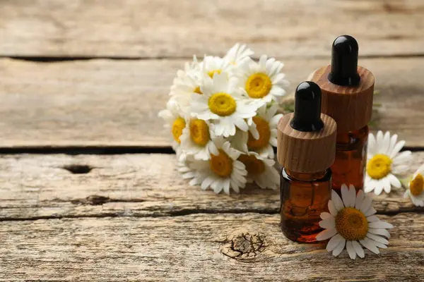 Ahşap masada gerekli yağ şişeleri ve papatya çiçekleri, yakın plan. Metin için boşluk