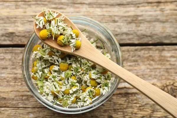 Kuru papatya çiçekleri kâsede ve kaşık tahta masada, üst tarafta.