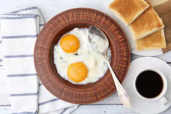 Tabakta yarı haşlanmış yumurta, kahve ve kızarmış ekmek beyaz ahşap masada, düz yatıyordu.