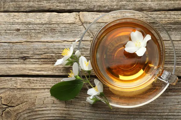 Cam bardakta Aromatik yasemin çayı, çiçekler ve ahşap masada yeşil yaprak, düz yatak. Metin için boşluk