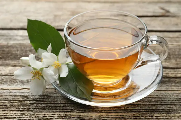 Cam bardakta yasemin çayı, ahşap masada çiçekler ve yeşil yapraklar, yakın plan.