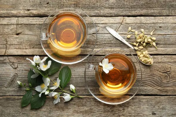 Cam bardaklarda yasemin çayı, tahta masada çiçekler ve yeşil yapraklar.