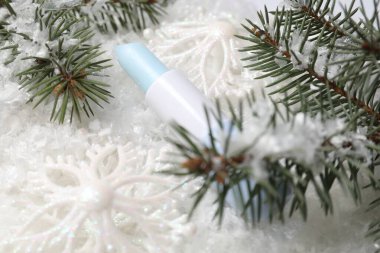 Nemlendirici dudak kremi, Noel dekorasyonu ve yapay kar üzerindeki köknar ağacı dalları, yakın plan. Kış bakımı