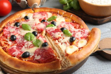 Gri ahşap masada salamlı, peynirli, fesleğenli ve zeytinli lezzetli pizza.