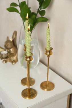 Zarif şamdanlar, yanan mumlar, vazoda dallar ve bej duvarın yanındaki şifoniyerde diğer dekorlar.