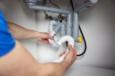 Tesisatçı, lavabonun altındaki boruları tamir ediyor. Kapalı.