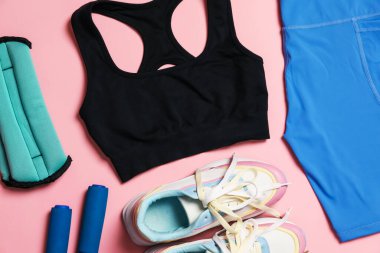 Spor kıyafetleri, bilek ağırlıkları, ip atlama ve pembe arka planda spor ayakkabıları, düz uzanma.