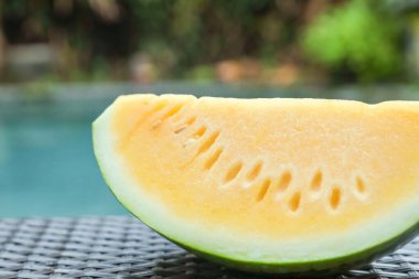 Açık havuz kenarında hasır masada lezzetli bir karpuz dilimi, yakın plan.