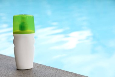 Yüzme havuzunun yakınındaki taş yüzeyde bir şişe güneş koruması ürünü, metin için yer