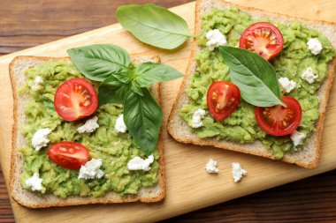 Avokado, domates, fesleğen ve peynirli nefis sandviçler ahşap masanın üstünde.
